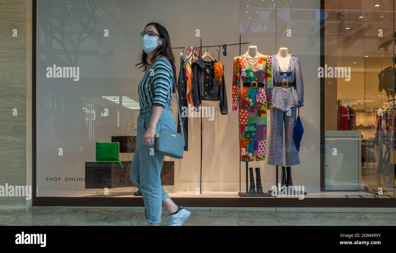 Una giovane donna che indossa una maschera per il viso passa davanti a una finestra di un negozio di abbigliamento in un centro commerciale a Città del Messico durante la pandemia di Covid-19 Foto Stock