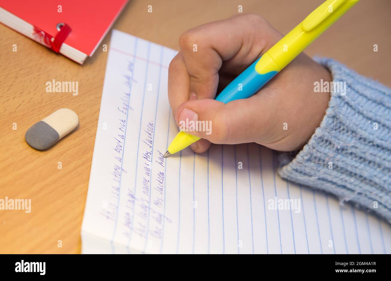 Le mani degli allievi in primo piano stanno scrivendo in inglese con una  penna a sfera. Uno scolaro svolge un compito sul posto di lavoro. Il  concetto di educazione dei bambini, di
