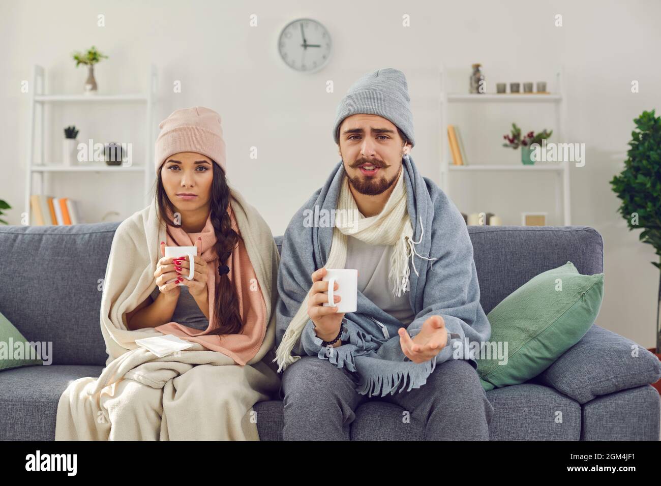 La giovane coppia malata davanti alla webcam si siede avvolta in coperte con una tazza di tè. Foto Stock