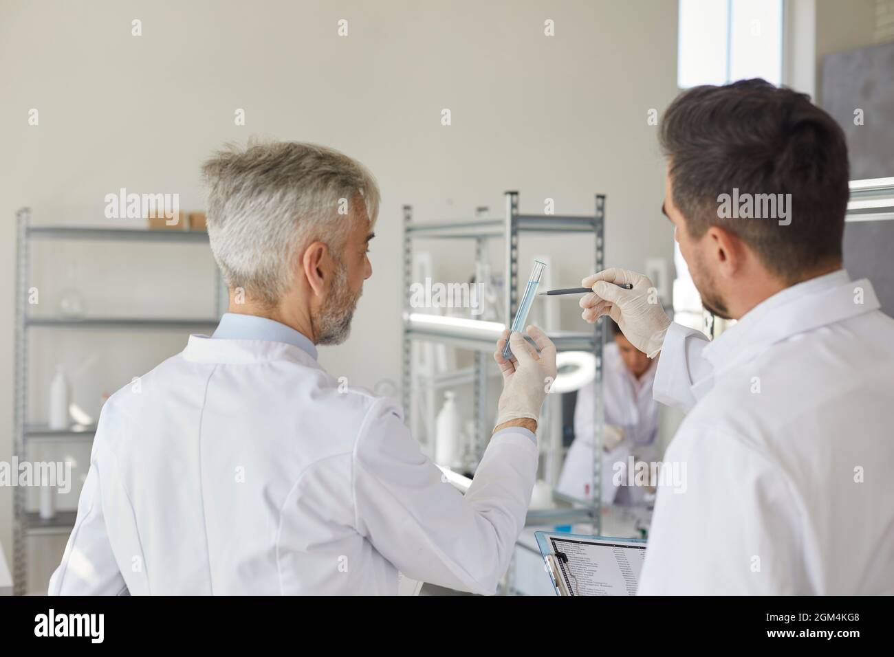 Due scienziati maschi, in piedi con le spalle alla telecamera, guardano una provetta con liquido. Foto Stock