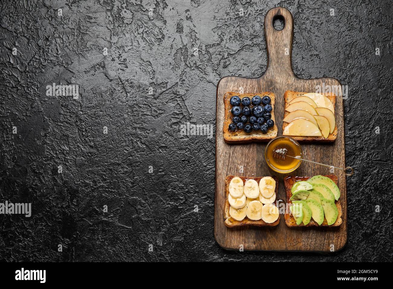 Delizioso pane tostato con miele e frutta su sfondo nero Foto Stock