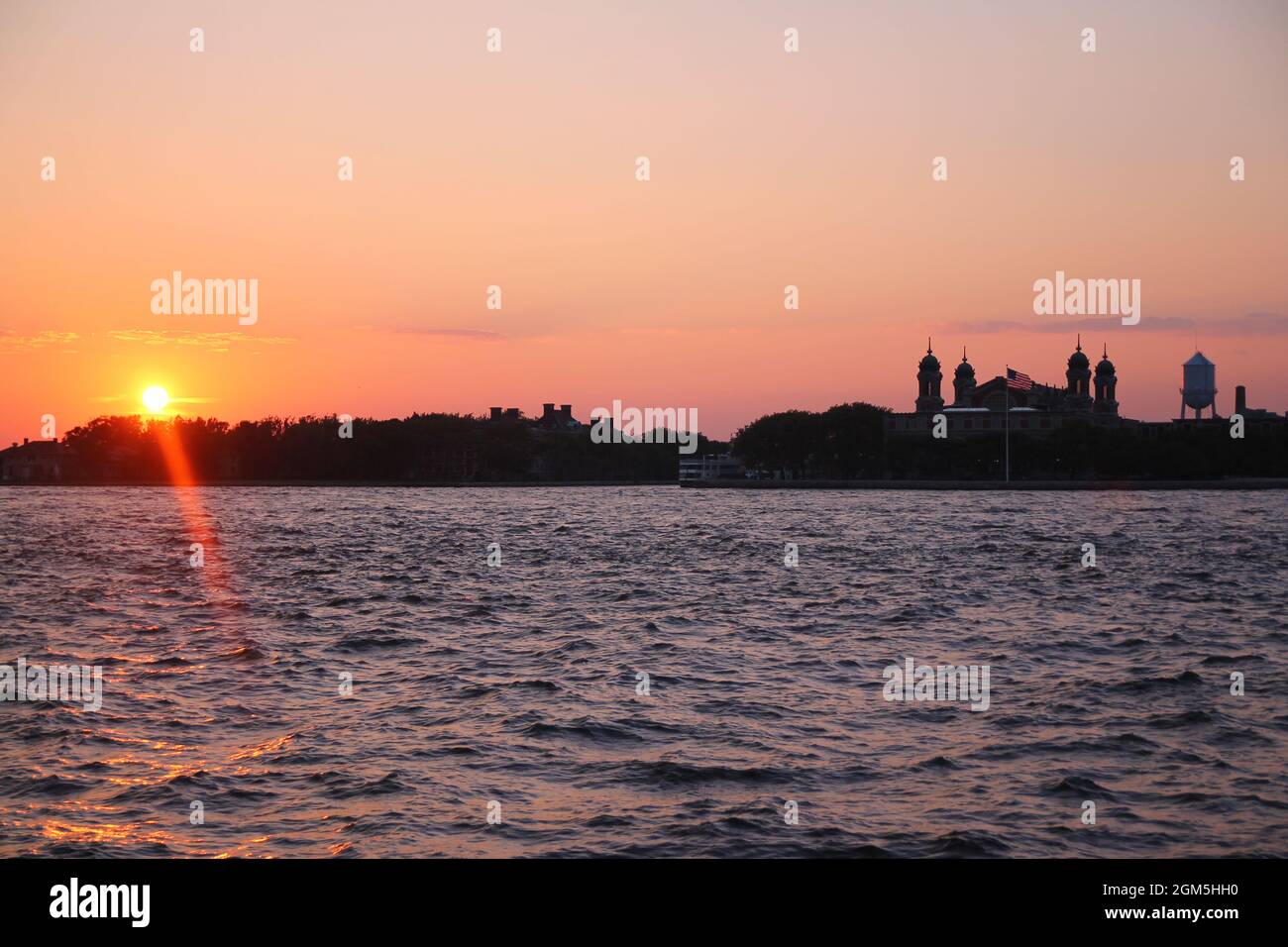 Il tramonto arancione dietro la storica Ellis Island a New York City Foto Stock