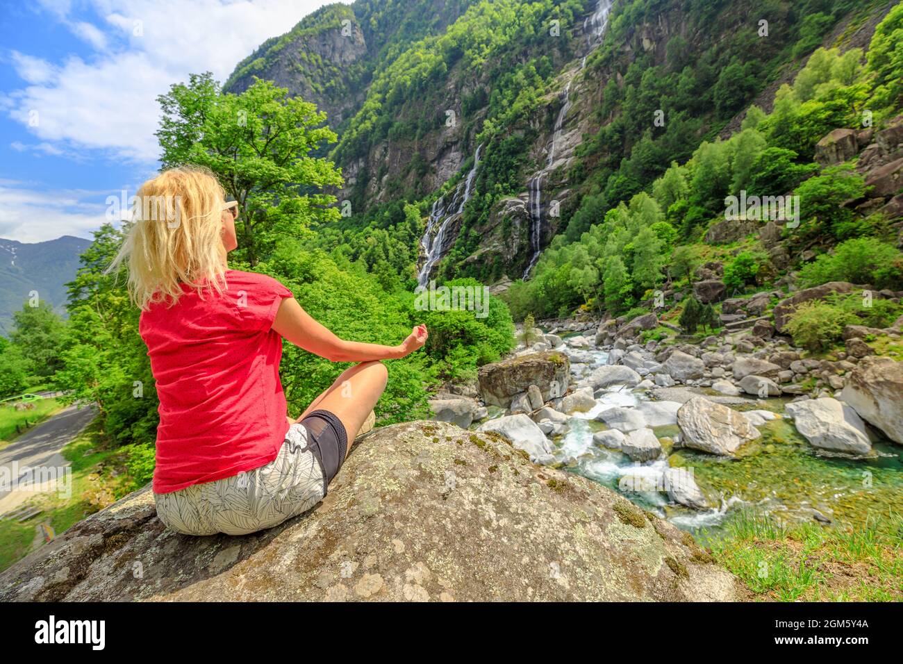 Donna tranquilla che fa meditazione yoga in posa di loto al bordo del vecchio ponte di pietra romana Steinbrucke sul fiume Bavona. Guardando la cascata Foto Stock