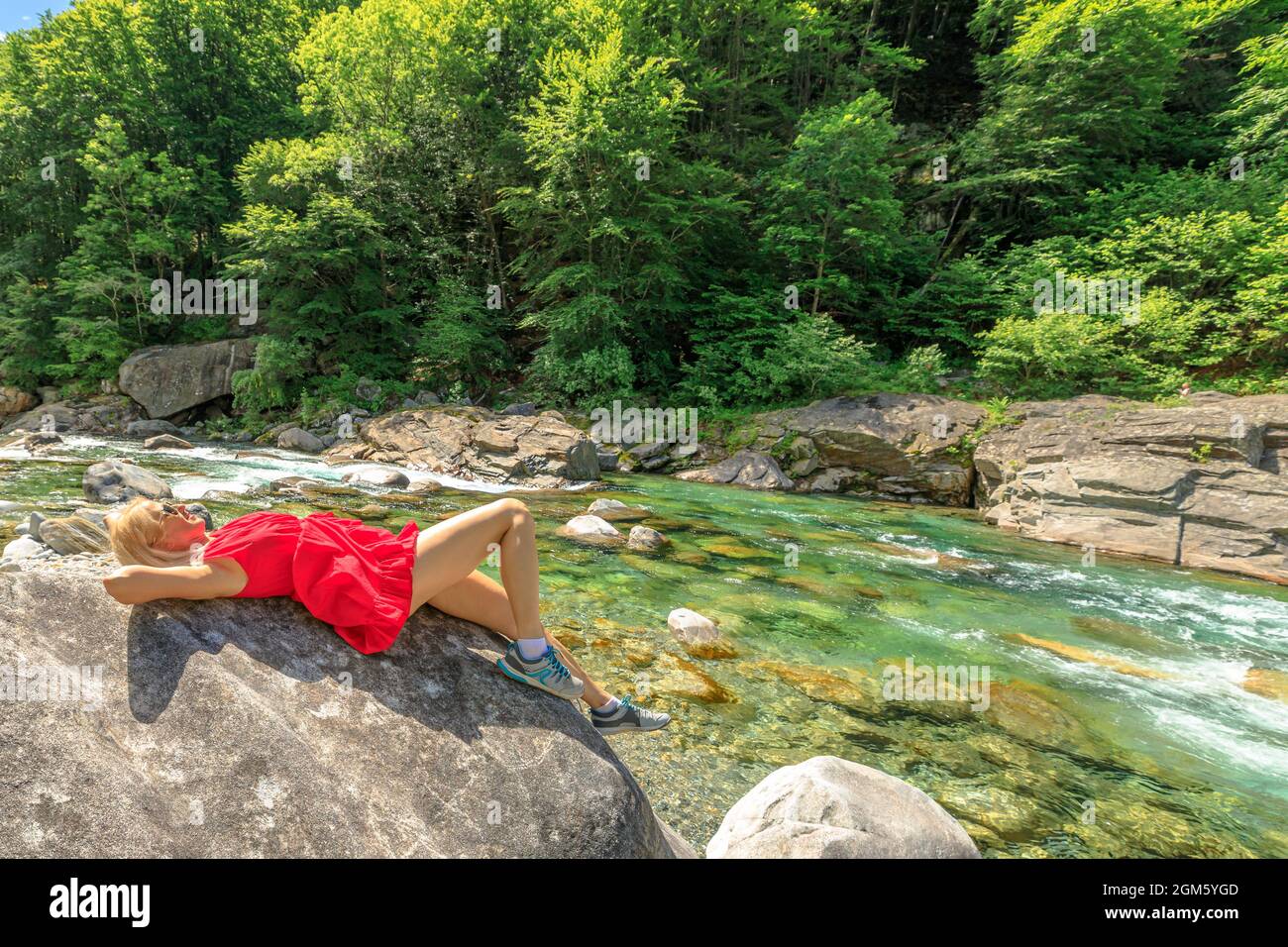 Donna seduta rilassante sulle rocce del fiume Verzasca. Valle Verzasca per la città di Lavertezzo. Famoso punto di riferimento per lo svago sul fiume e le immersioni Foto Stock