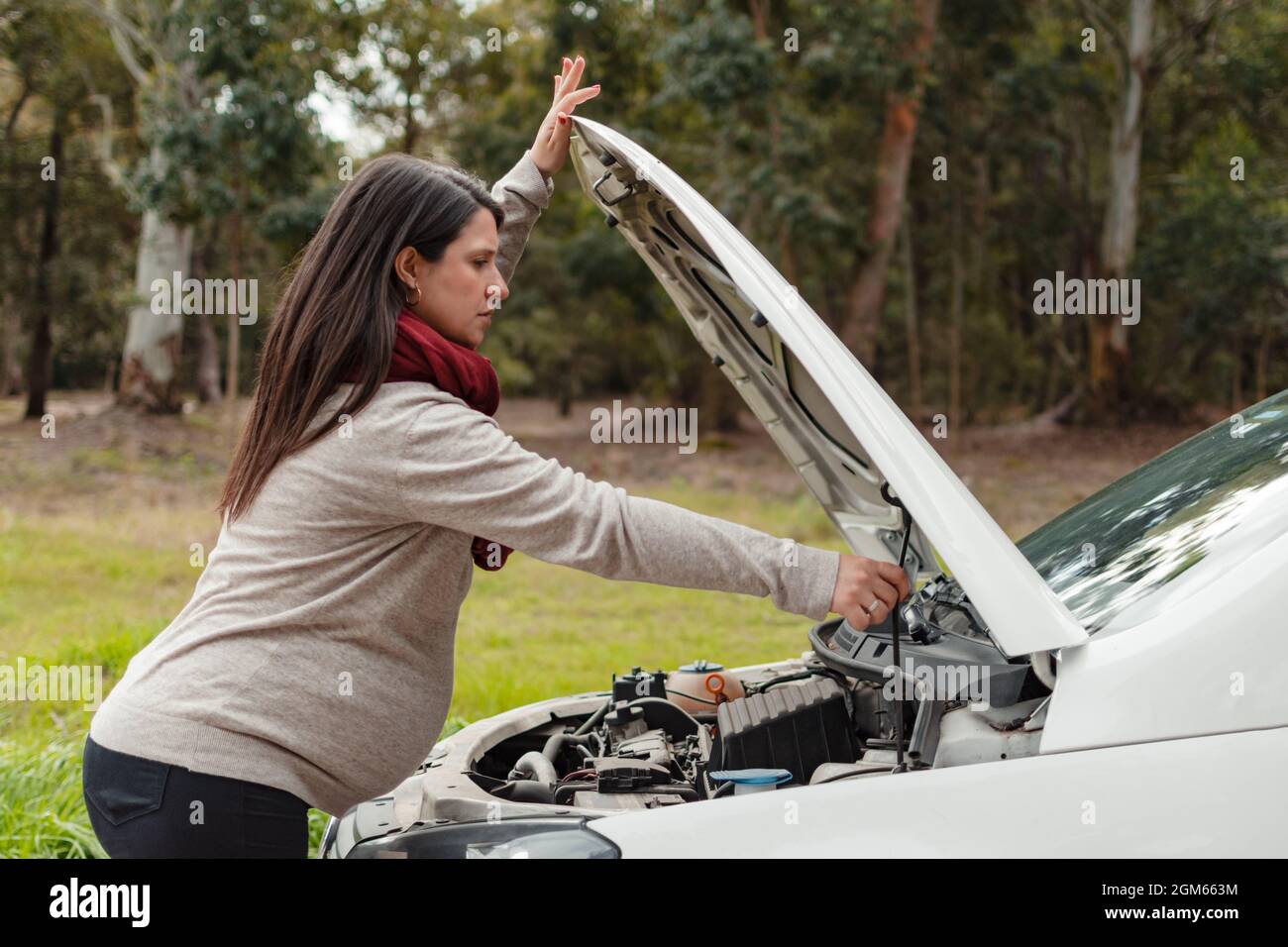 donna di latina incinta che chiude o apre il cofano della sua auto Foto Stock