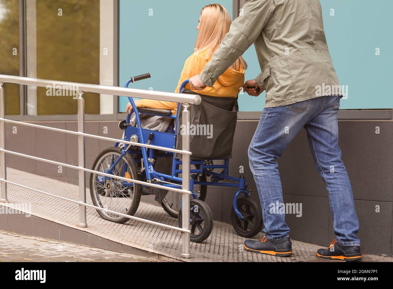 Uomo con la moglie in sedia a rotelle sulla rampa all'aperto Foto Stock
