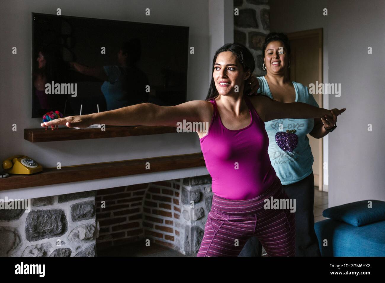 Giovane ispanica che fa yoga con istruttore femminile che regola la sua postura a casa in Messico Foto Stock