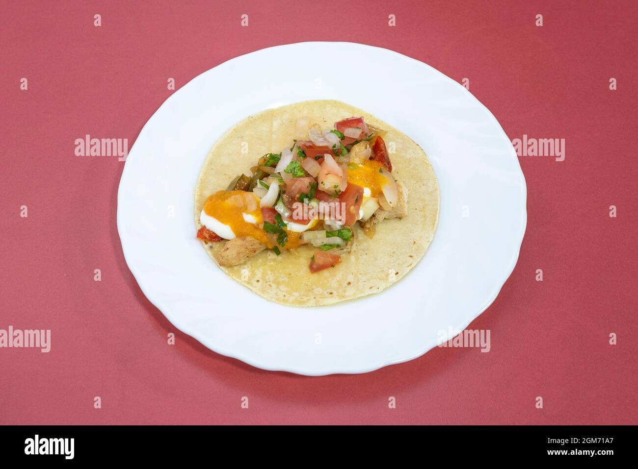 taco messicano con fajita ripieno di pico de gallo, carne di pollo stufata su piatto bianco e sfondo rosso Foto Stock taco messicano con fajita ripieno di pico de gallo, carne di pollo stufata su piatto bianco e sfondo rosso Foto Stock
