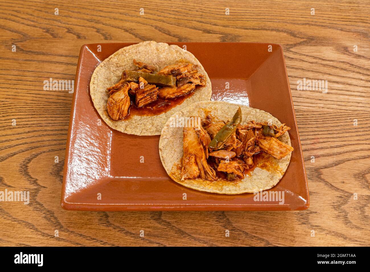 Tacos messicani con tortillas di farina di grano e mixiote di pollo con nopales su un piatto quadrato di terracotta Foto Stock Tacos messicani con tortillas di farina di grano e mixiote di pollo con nopales su un piatto quadrato di terracotta Foto Stock