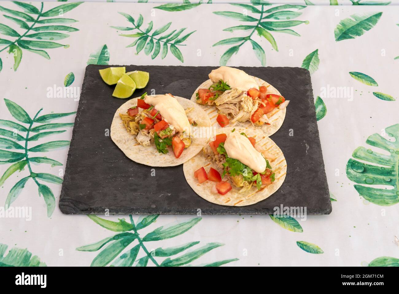 Tre tacos in tortilla di grano con un ripieno di pollo tirato, maionese, pico de gallo, coriandolo e pezzi di lime su un piatto di ardesia nera Foto Stock Tre tacos in tortilla di grano con un ripieno di pollo tirato, maionese, pico de gallo, coriandolo e pezzi di lime su un piatto di ardesia nera Foto Stock