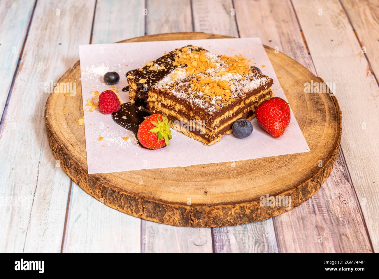 deliziosa e colorata porzione di torta di nonna con tre strati di cioccolato e tre strati di biscotto, cocco grattugiato sulla parte superiore e bacche su Foto Stock