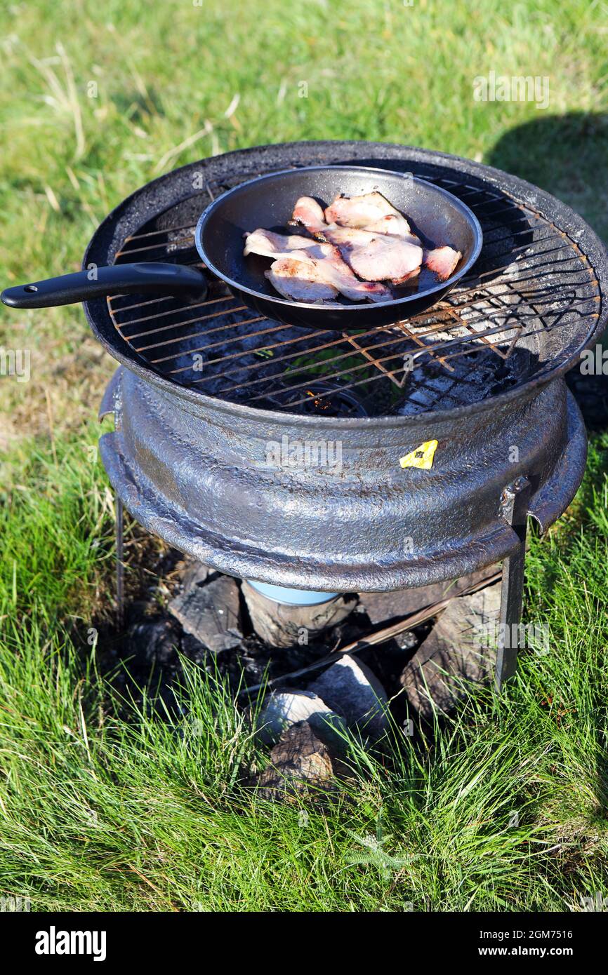 Frittura di pancetta su un barbecue all'aperto fatto da un cerchio di ruota scartato da un'auto Foto Stock
