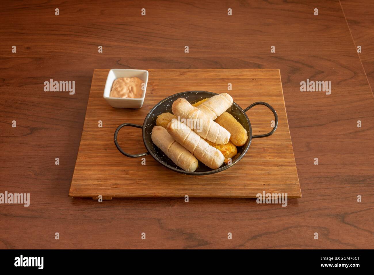 Servire di tequeños di vari sapori in una mini padella nera e salsa per un tuffo su un bordo di bambù Foto Stock