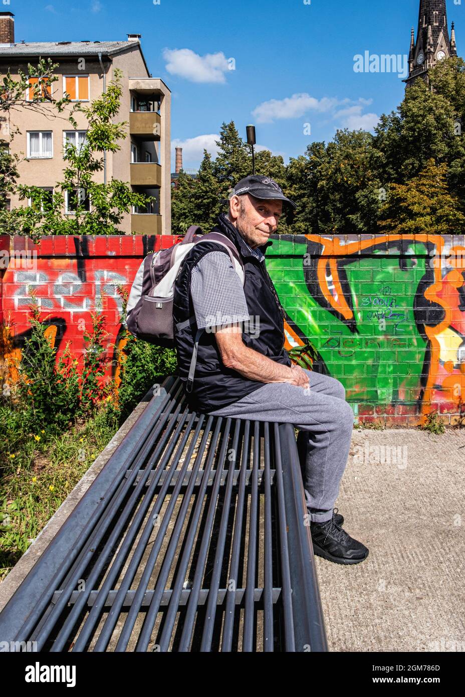 L'uomo anziano siede sul banco accanto al muro divisorio iin Nordbahnhof Park che si trova sul muro di Berlino, Mitte, Berlino Foto Stock