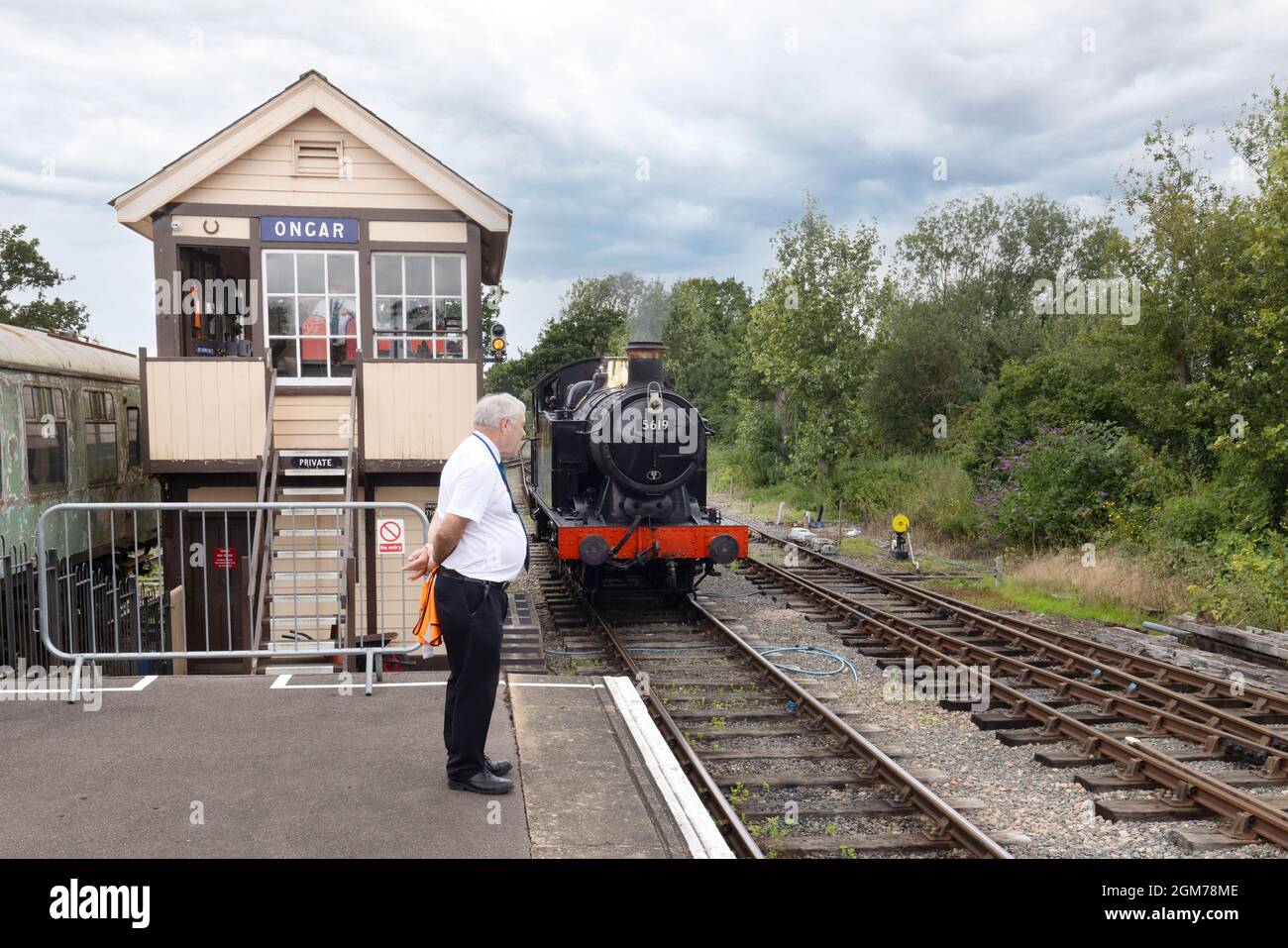 Treno a vapore Regno Unito - locomotiva a vapore che si avvicina alla stazione di Ongar, con segnale box e stationmaster in presenza, Epping-Ongar Heritage Railway Essex UK Foto Stock