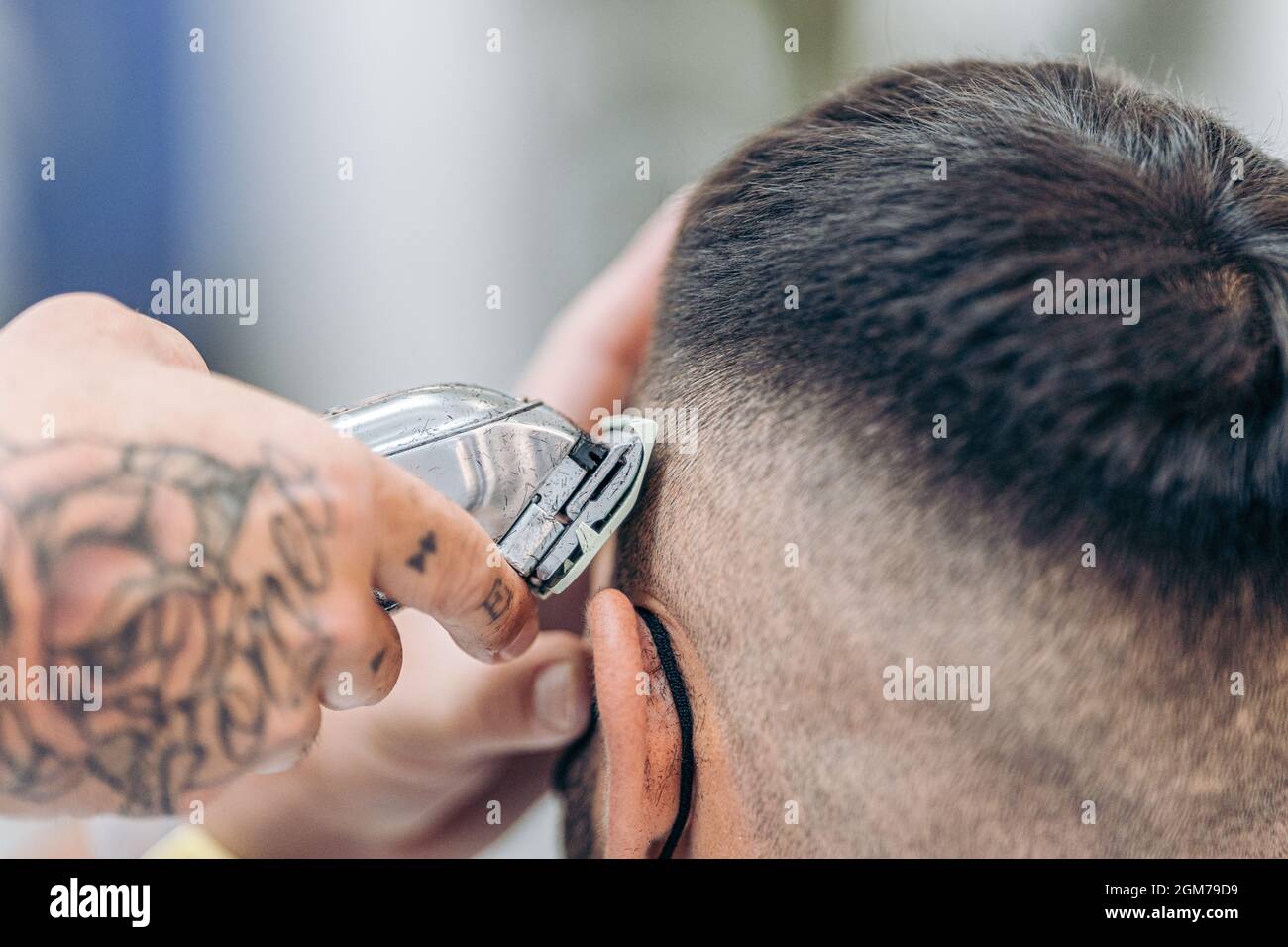 Mano tatuata con una macchina da rasatura per tagliare i capelli di un  cliente in un barbiere Foto stock - Alamy