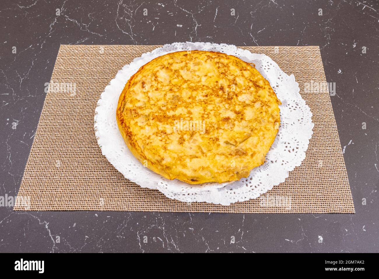 Grande frittata spagnola con uova e patate con cipolla su un vassoio di pasticceria con carta perforata Foto Stock