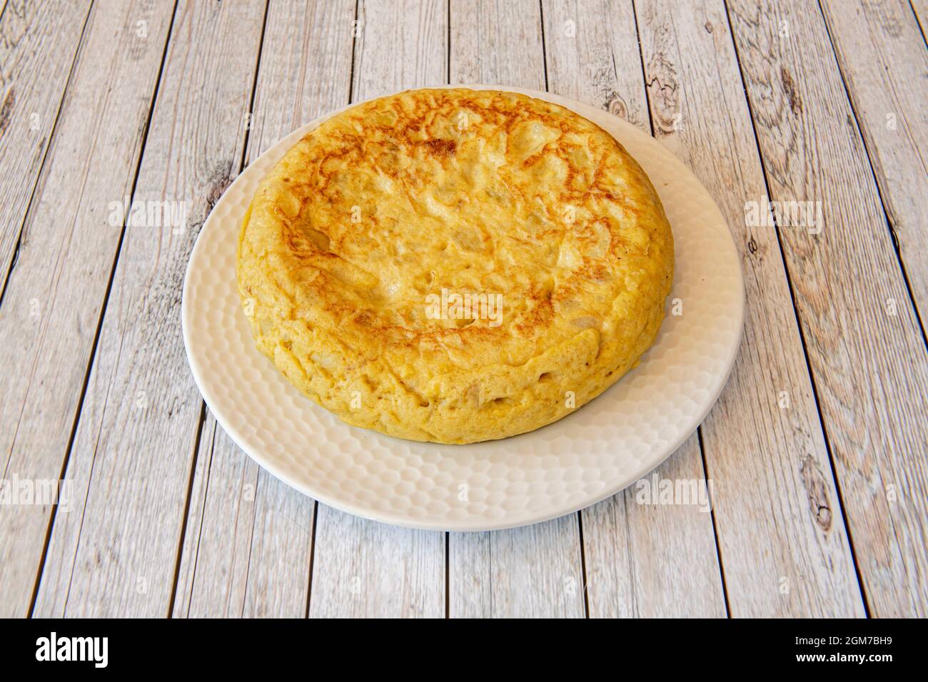 Frittata spagnola con patate e uova di notevole spessore su un piatto bianco e un tavolo di legno chiaro Foto Stock