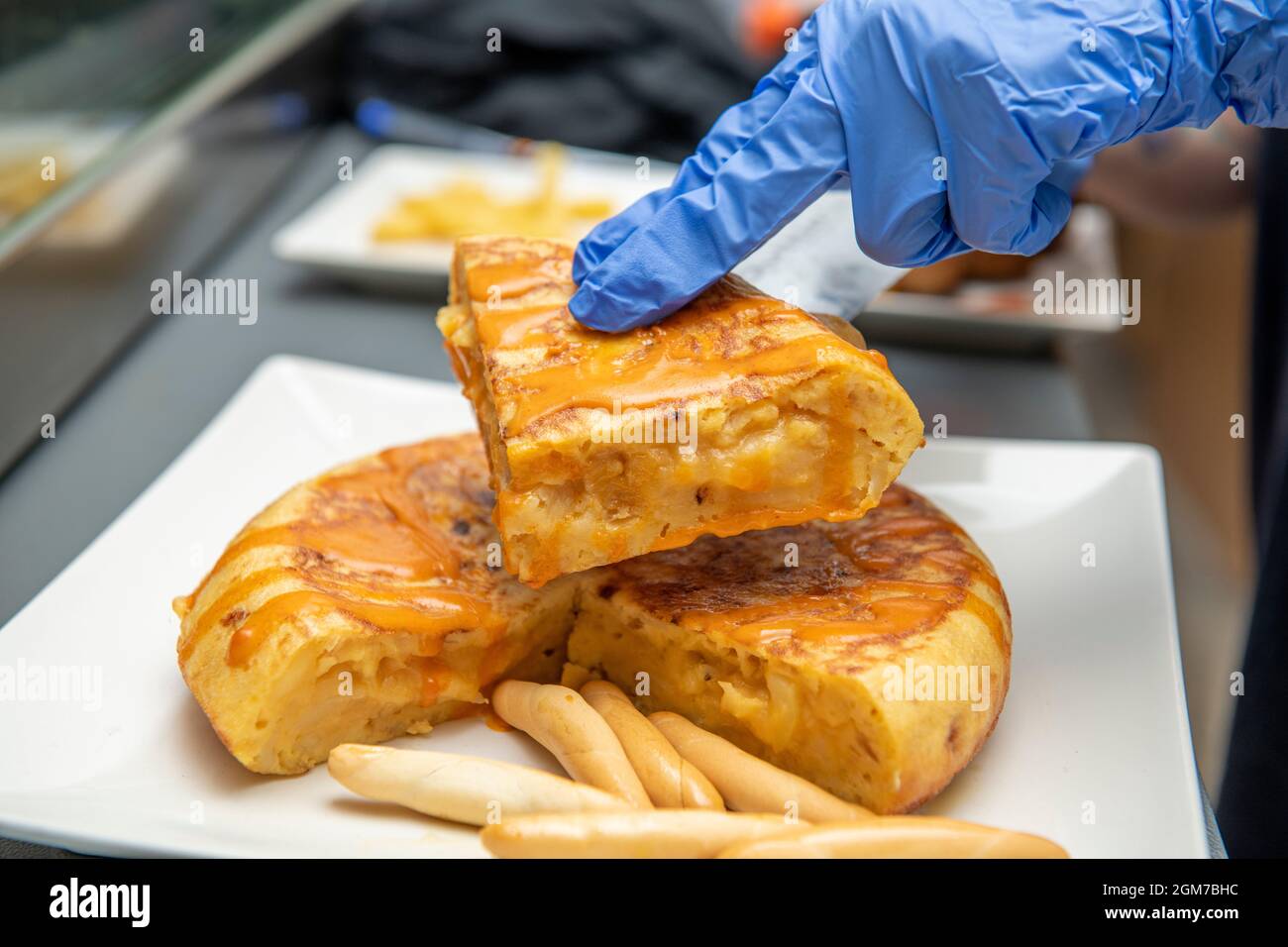 Le mani guanto separano un pezzo di tortilla per fare una tapa spagnola con cime di campagna Foto Stock