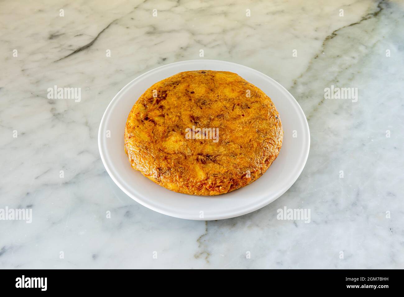 Frittata spagnola con un sacco di succo servito su un piatto bianco su un tavolo di marmo bianco Foto Stock