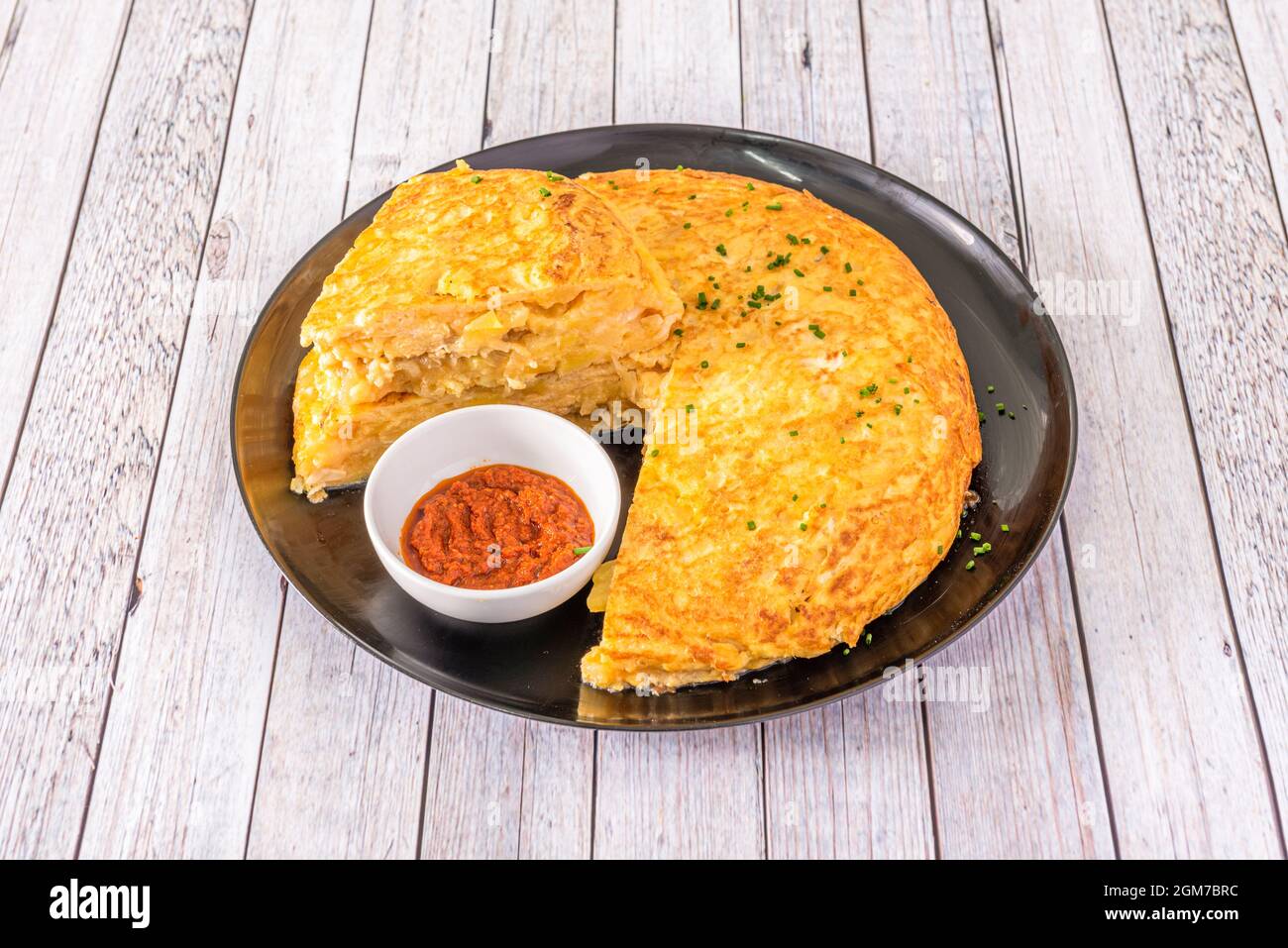 Frittata spagnola con formaggio e cipolla e salsa di peperoni rossi su piatto nero circolare Foto Stock