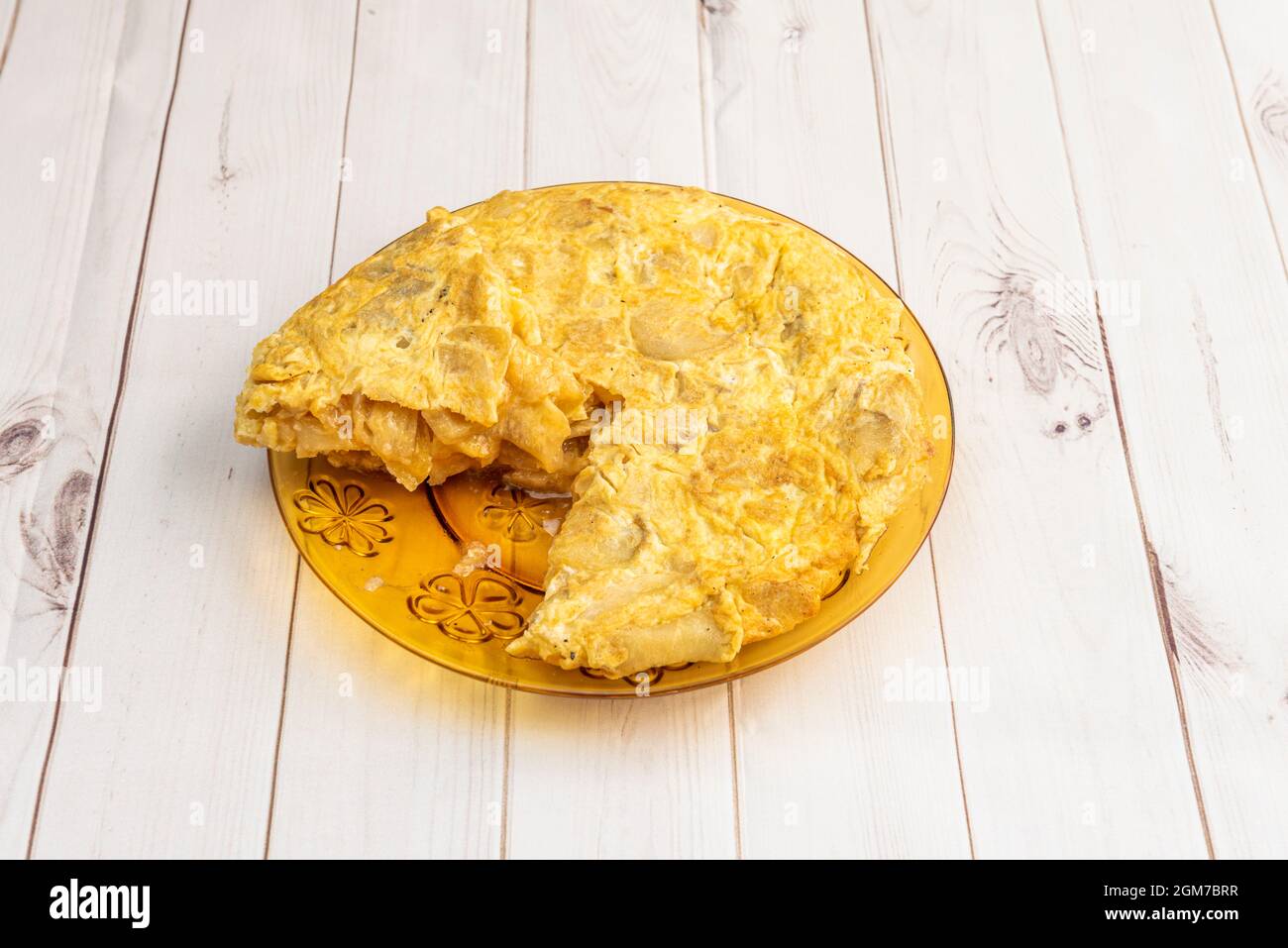 Omelette di patate spagnole fatte in casa leggermente arricciate al gusto dei commensali che preferiscono poco cotto su un piatto di duralex e un tavolo bianco Foto Stock