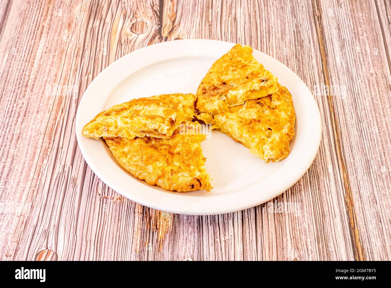 Omelette a farfalla. Frittata spagnola con uova su piatto bianco e tavolo di legno rossastro. Foto Stock