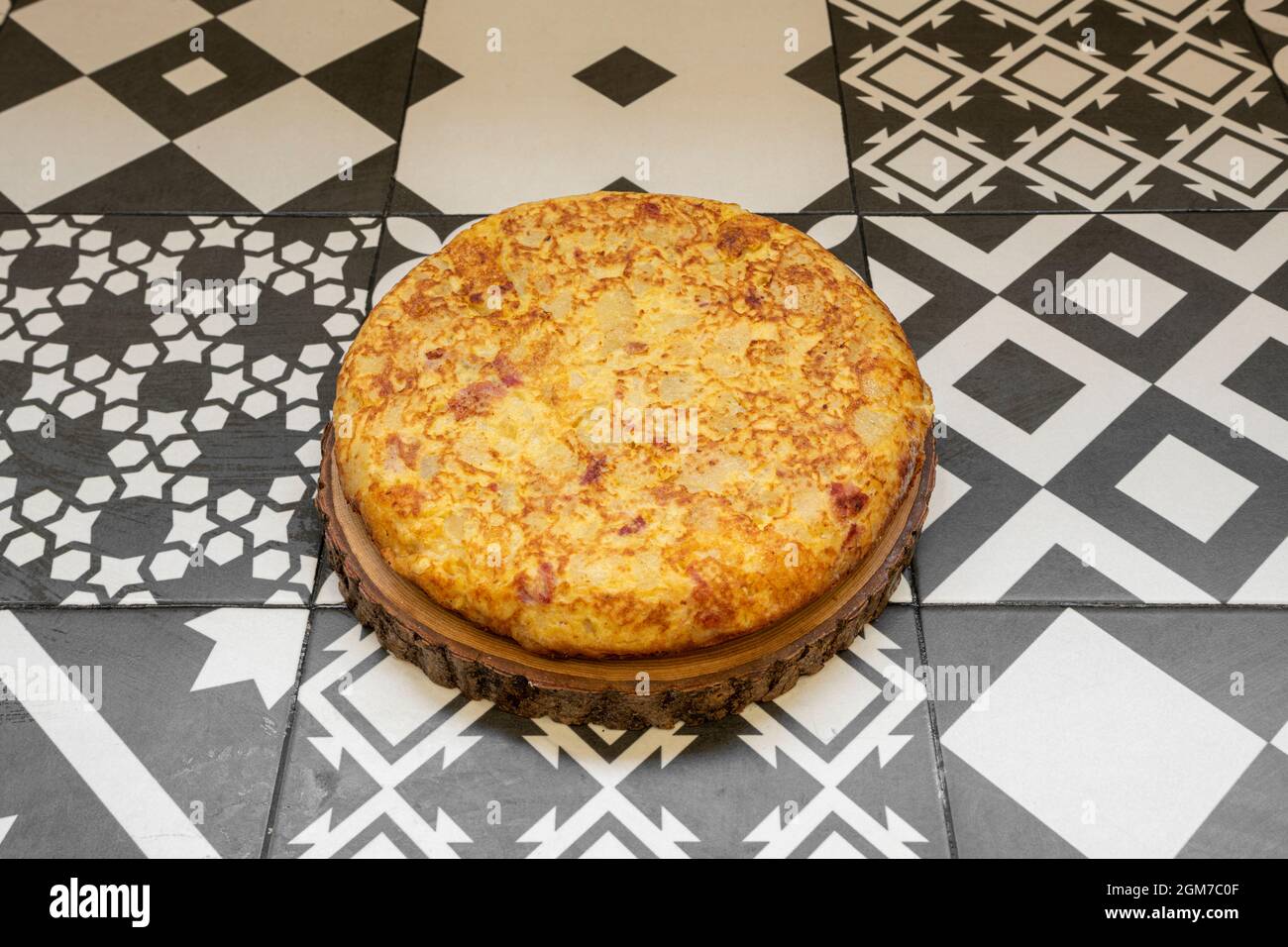 Frittata spagnola per quattro con pezzetti di pancetta su un tronco di legno Foto Stock