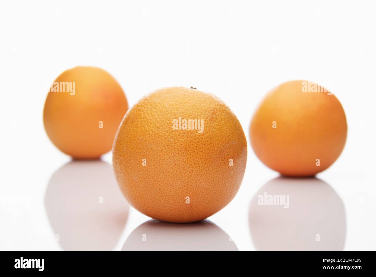 Tre pompelmi arancioni interi isolati su sfondo bianco, due di loro sono fuori fuoco, bokeh Foto Stock