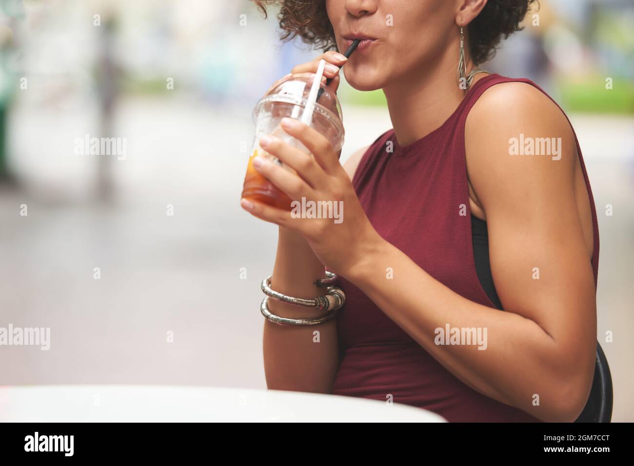 Immagine ritagliata di una giovane donna che sorseggia una deliziosa bevanda a base di frutta quando si siede al tavolo del caffè all'aperto Foto Stock