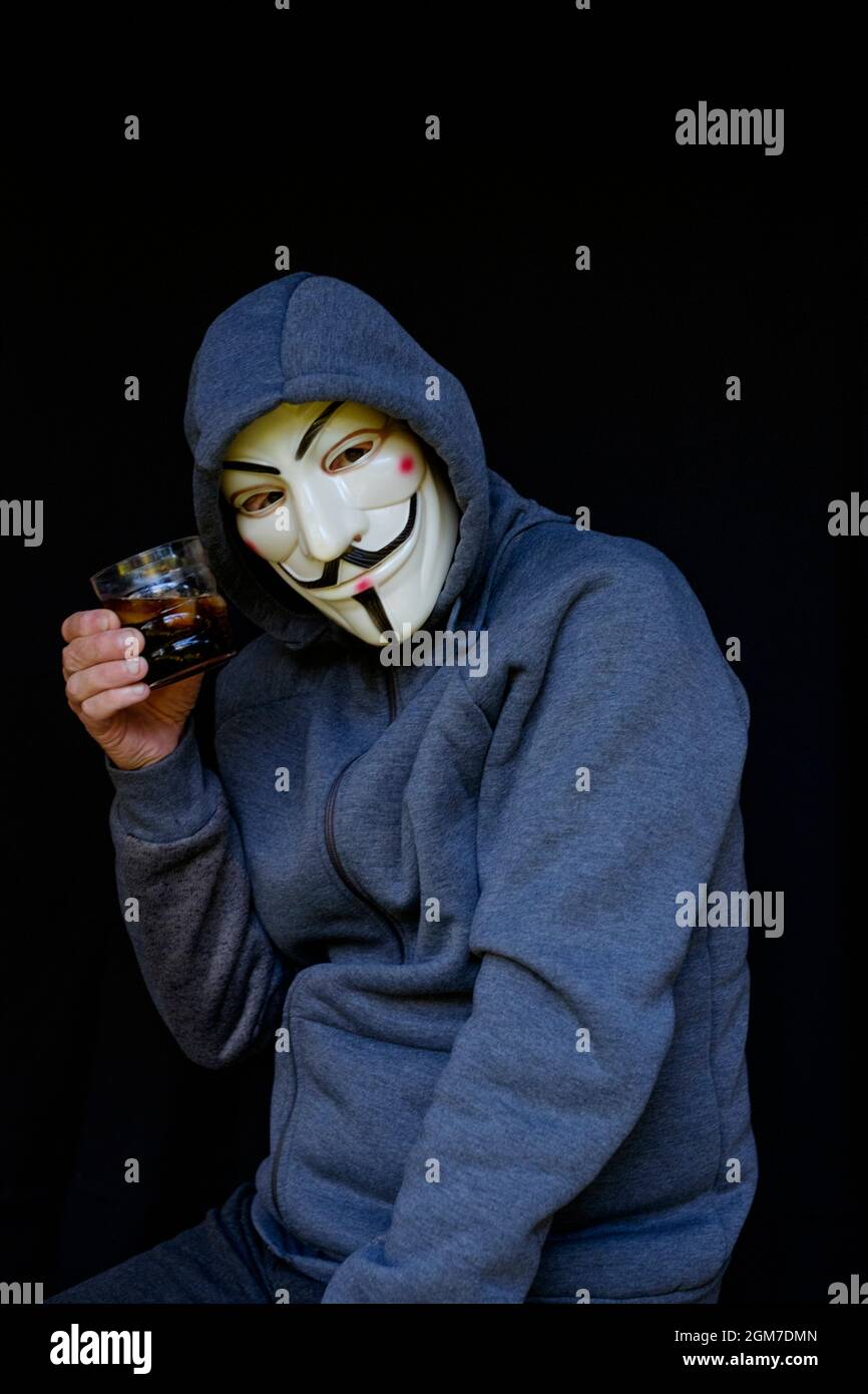 anti vaccino maschio cospirazione teorico indossare cappuccio e v per maschera di vendetta toasts con bicchiere di alcol Foto Stock