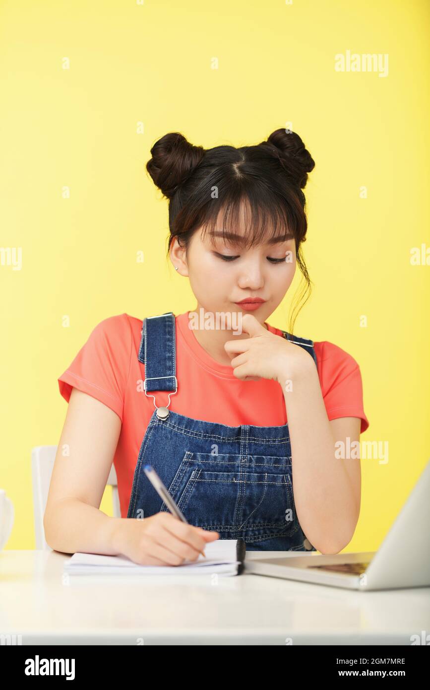 Pensivo giovane donna graziosa che scrive nel copybook quando fa i compiti di matematica e risolvendo le equazioni Foto Stock