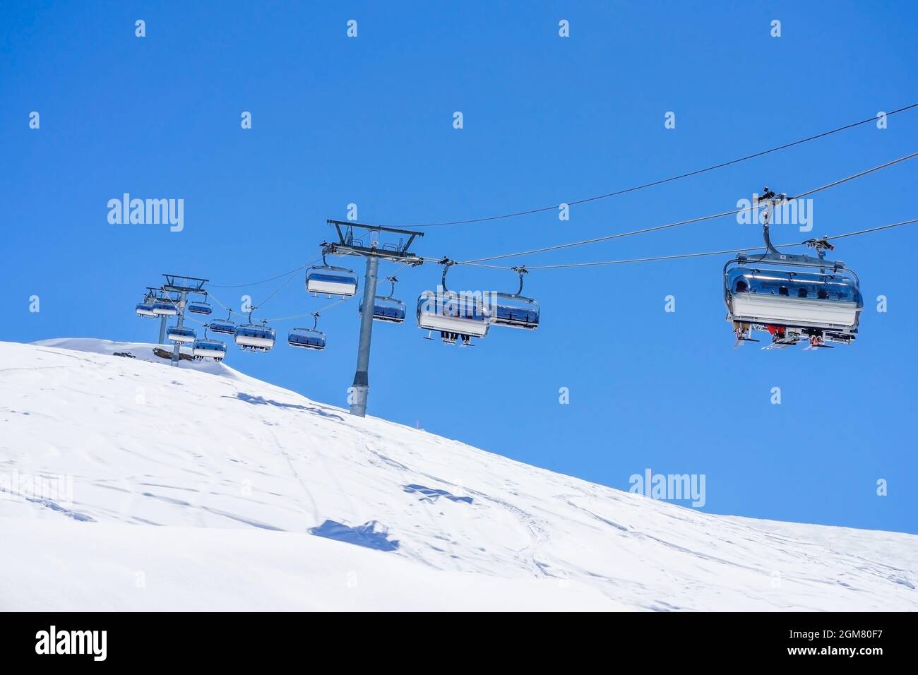 La gente si alza sugli impianti di risalita con posti a sedere che si snodano sulla montagna e sentieri da cieli e snowboard Foto Stock