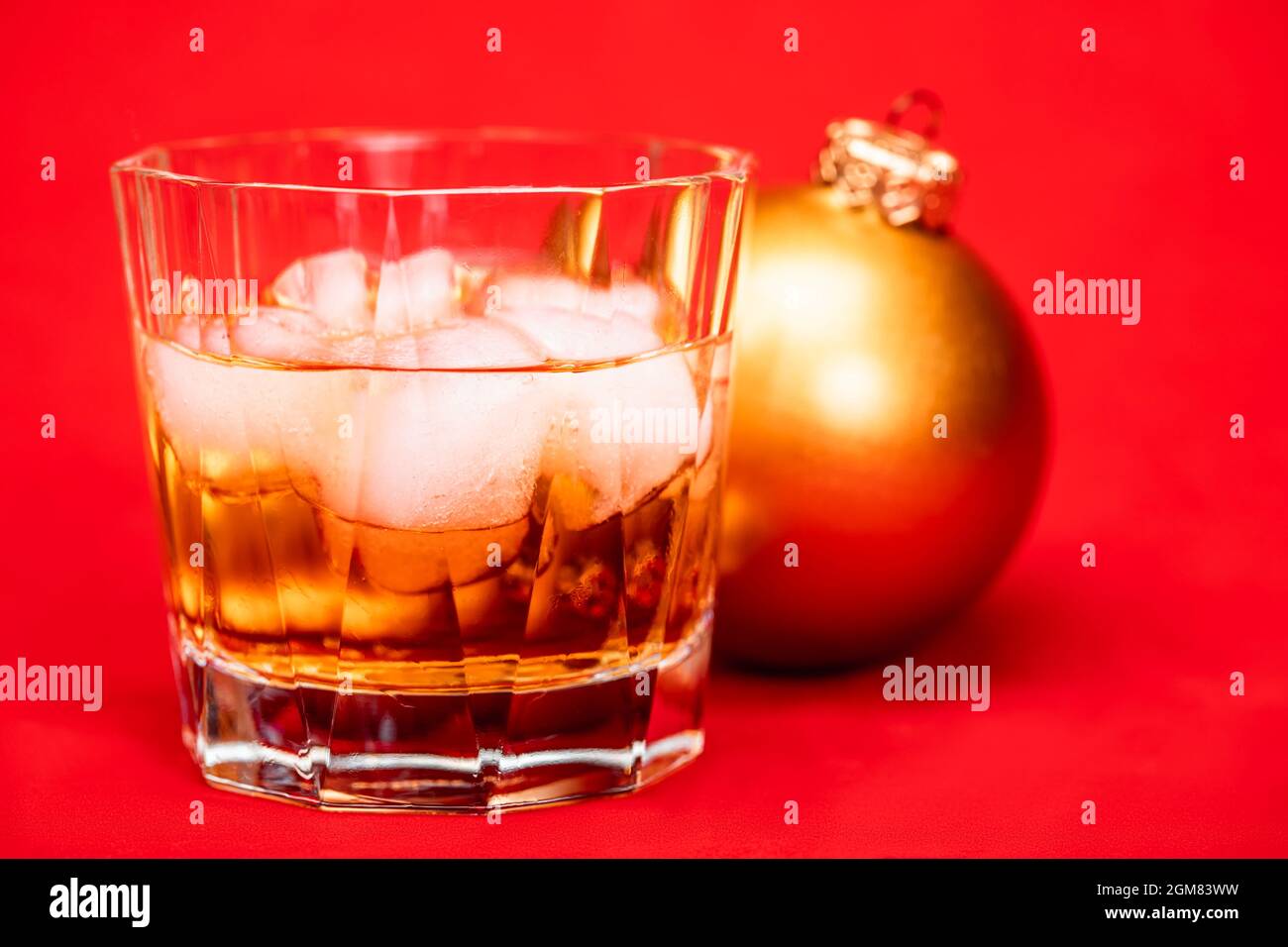 Bicchiere di whiskey con cubetti di ghiaccio e bauble di natale su sfondo rosso - concetto di bevanda di natale Foto Stock