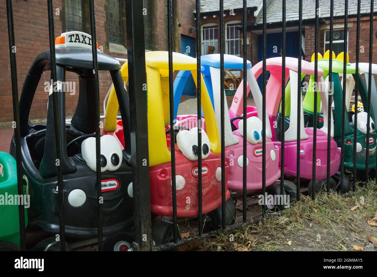 Primo piano di una fila di pedalate Little Tikes accoglienti carrozze a pedali Coupe che aspettano in un asilo nido, Londra, Inghilterra, Regno Unito Foto Stock