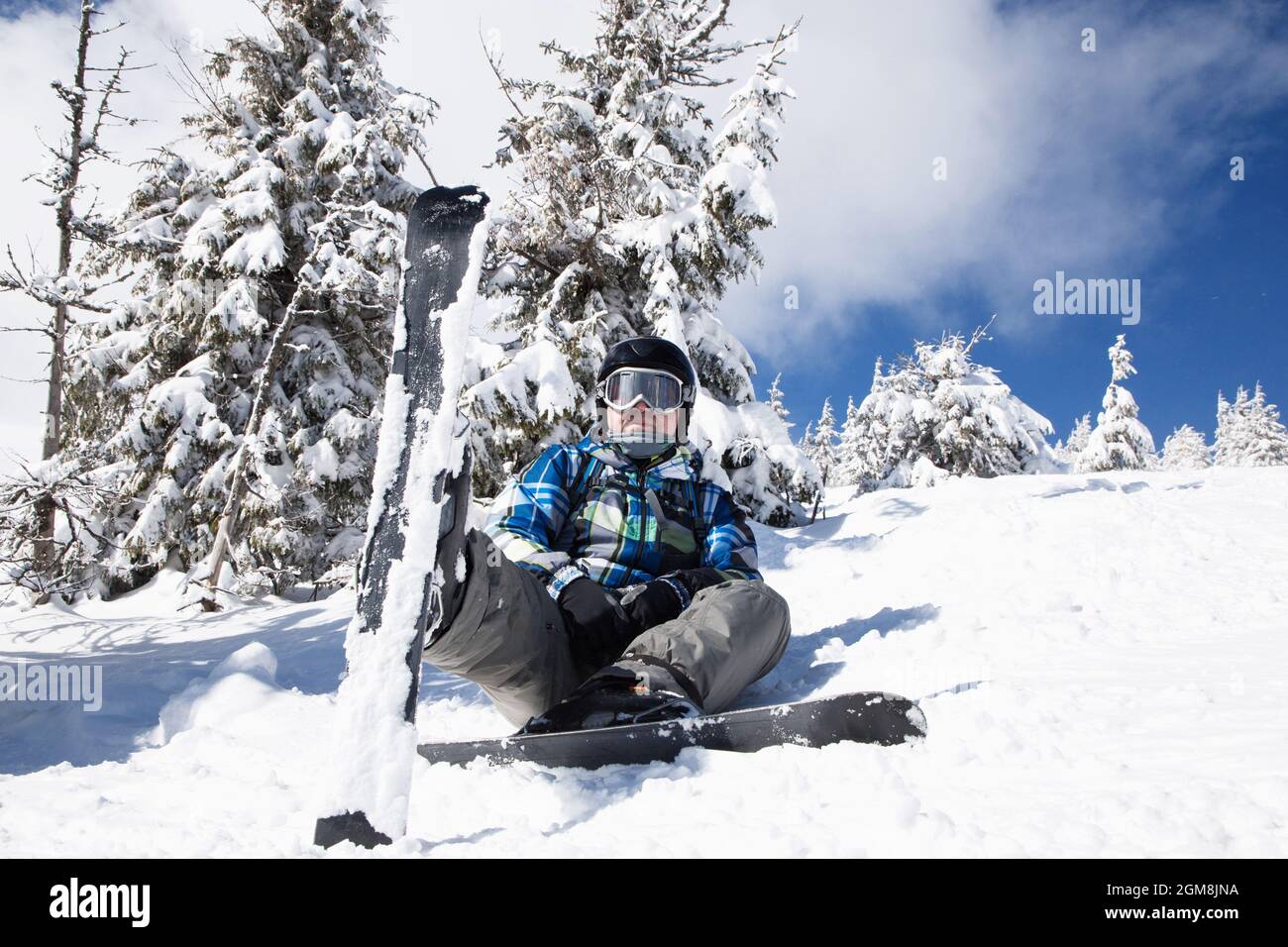 uomo di circa 35-40 anni in abiti invernali sugli sci si siede nella neve in una giornata invernale soleggiata. sciatore godendo le vacanze invernali su una pista nevosa, relax Foto Stock