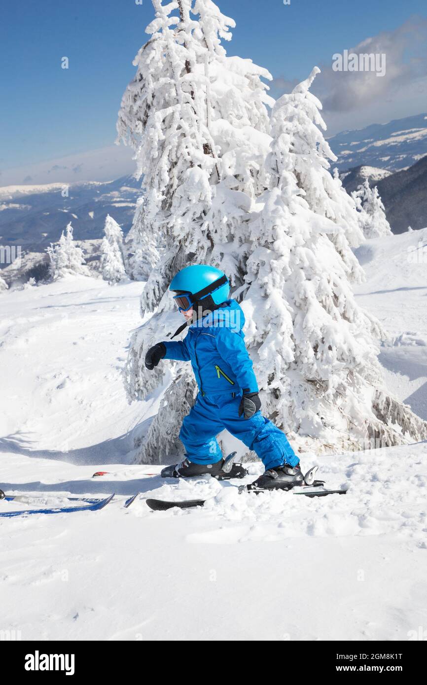 bambino ragazzo in casco, occhiali e tute blu sciare in belle montagne innevate. Animazione invernale attiva per bambini. Lezione di sci a un al Foto Stock
