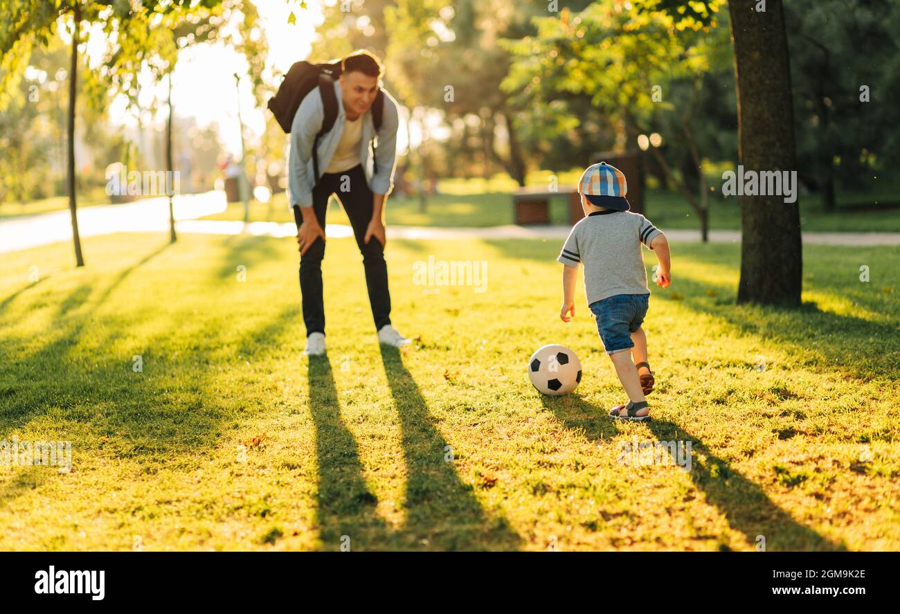 Felice ragazzino che gioca a calcio con suo padre, nel parco in una giornata di sole, si divertono mentre si fa jogging, famiglia, bambini, riposo Foto Stock