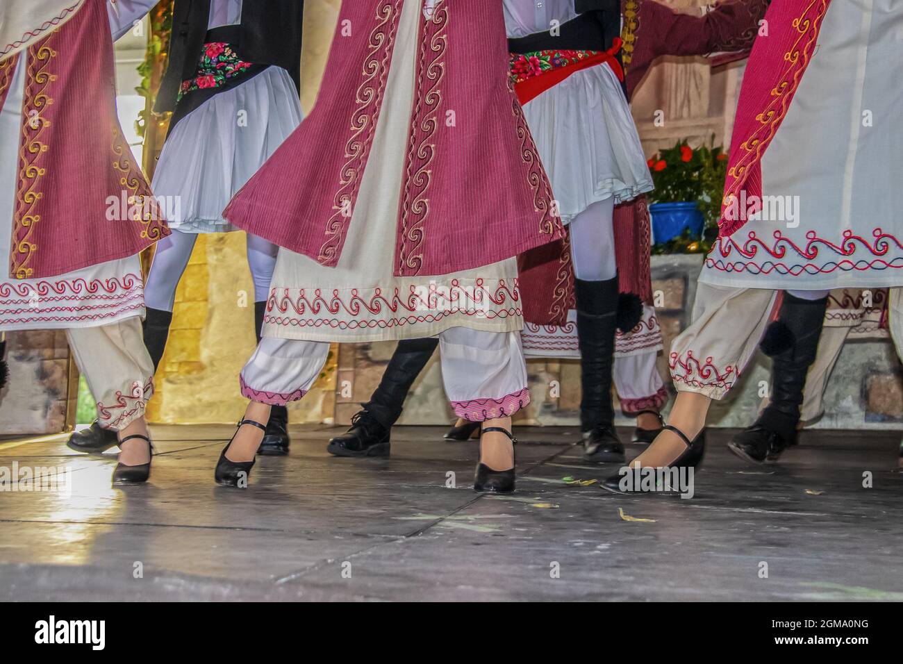 Vista ritagliata dei ballerini greci sul palco in bellissimo costume ricamato con le donne di fronte agli uomini - gambe e piedi - movimento sfocato Foto Stock
