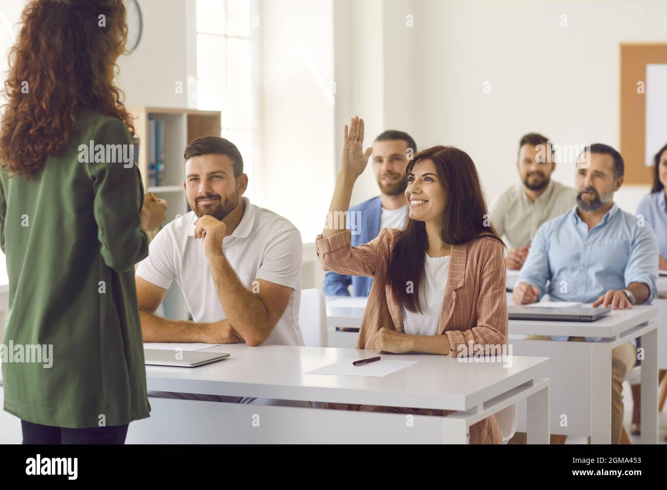 La donna felice alza la mano per fare all'insegnante una domanda durante un addestramento o un seminario Foto Stock