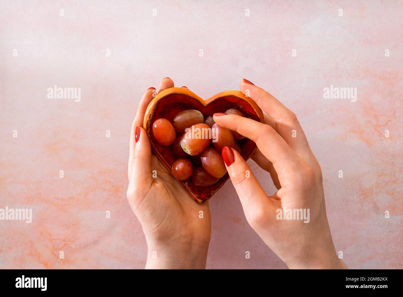 Le mani delle donne tengono un piatto a forma di cuore e selezionano un'uva. Tradizione spagnola di mangiare 12 uve a mezzanotte di Capodanno. Foto Stock