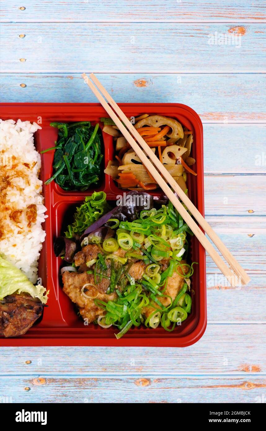 Scatola giapponese 'Makunouchi' bento con riso, cipolline, verdure e pollo. Sfondo tavola in legno. Foto Stock
