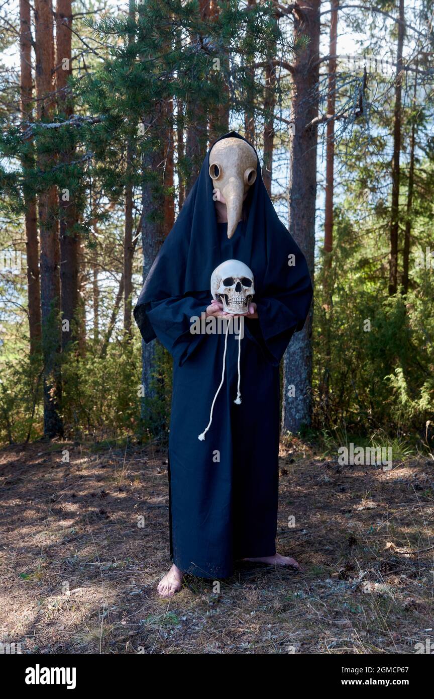 Un uomo che indossa una maschera medico peste si alza e tiene un cranio umano nelle sue mani Foto Stock