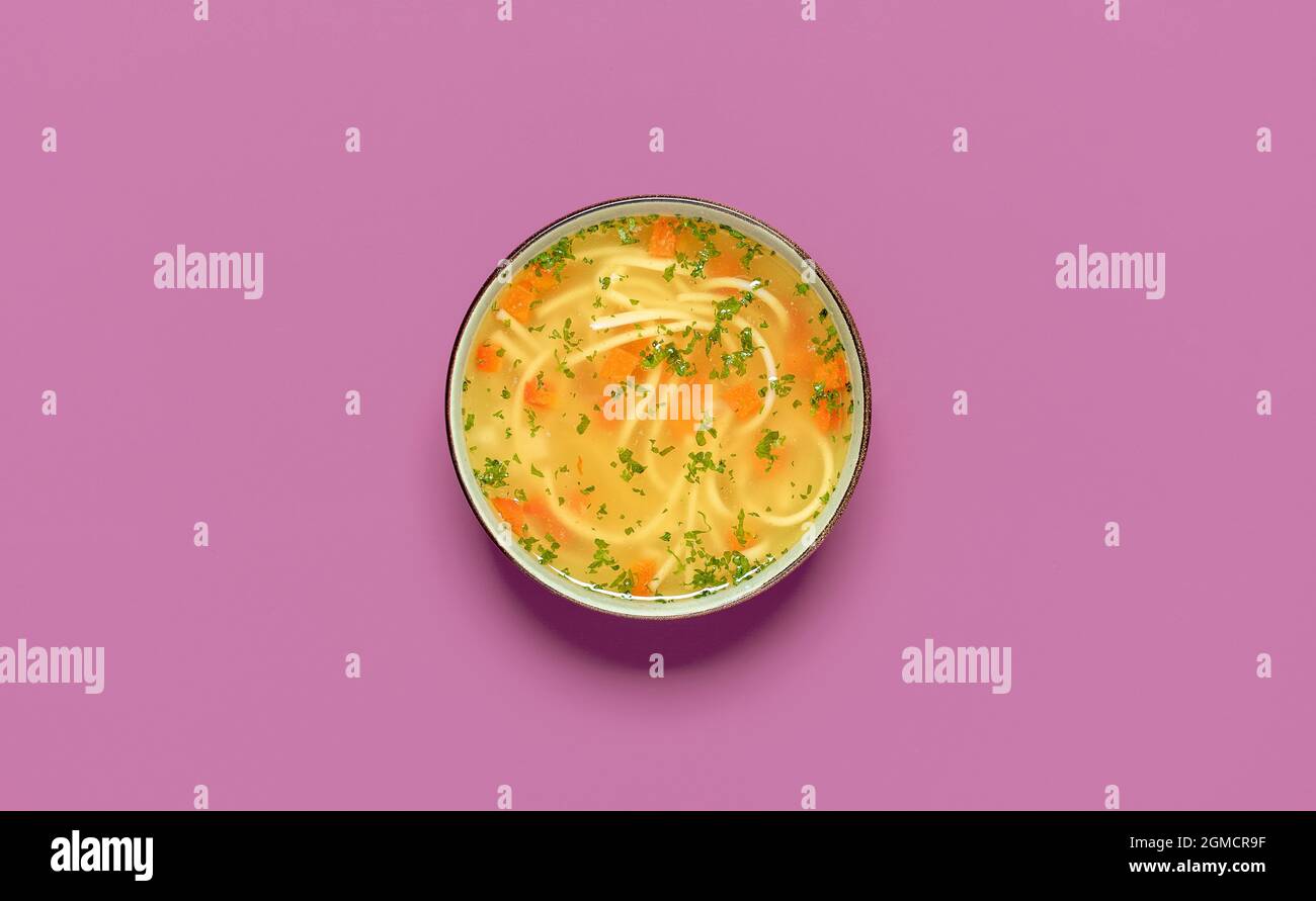 Vista dall'alto con una ciotola di zuppa di pollo isolata su sfondo viola. Deliziosa zuppa di pollo fatta in casa con verdure e spaghetti. Foto Stock