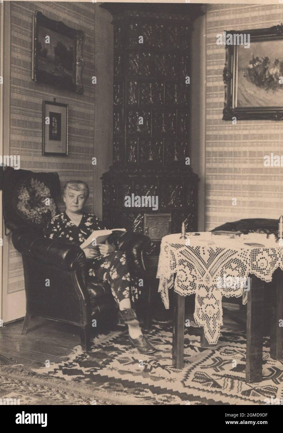 Foto vintage originale degli anni '1920 di una vecchia padrona di casa che legge nella sua poltrona in pelle Wingback in stile georgiano. E' seduta confortevole nella sua camera splendidamente decorata, circondata da molti dipinti. Forse era una collezionista d'arte / collezionista d'arte e casa Foto Stock