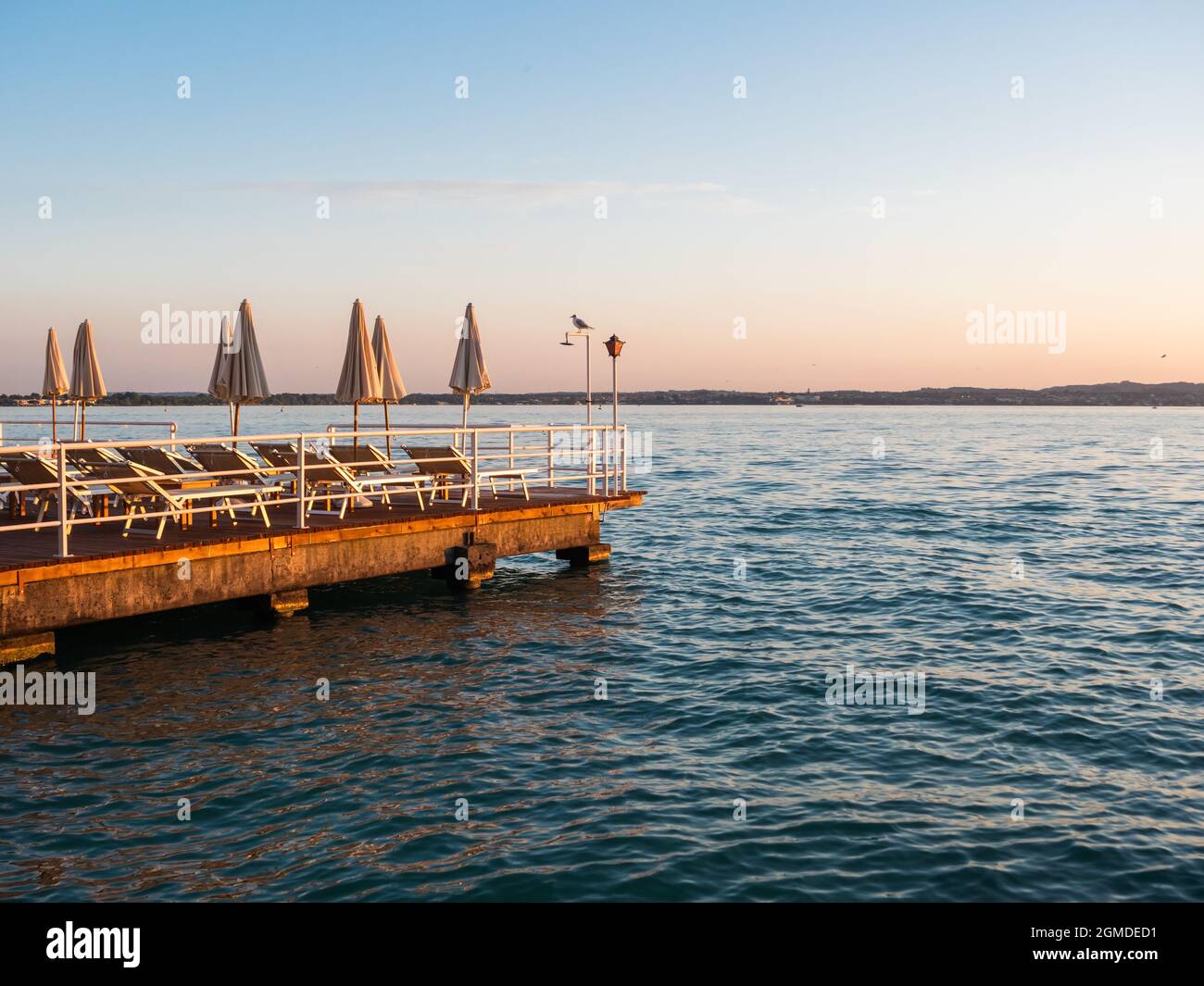 Piattaforma da bagno o terrazza con ombrelloni e sedie a sdraio al Lago di Garda a Sirmione in una serata estiva Foto Stock