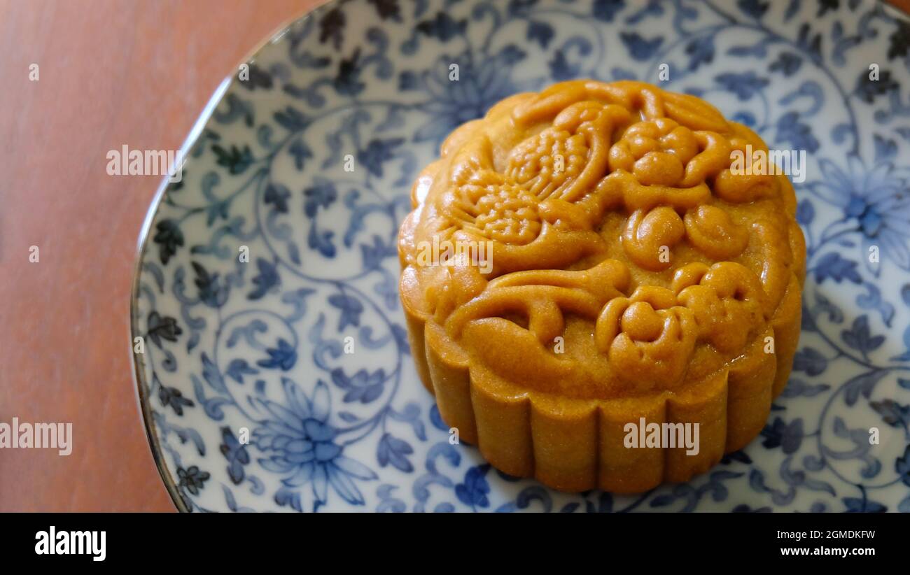 Primo piano di una torta di mooncake marrone con un bel motivo, posta su un piatto blu. Mooncake è un dolce cinese tradizionalmente consumato durante il Fe di metà-autunno Foto Stock