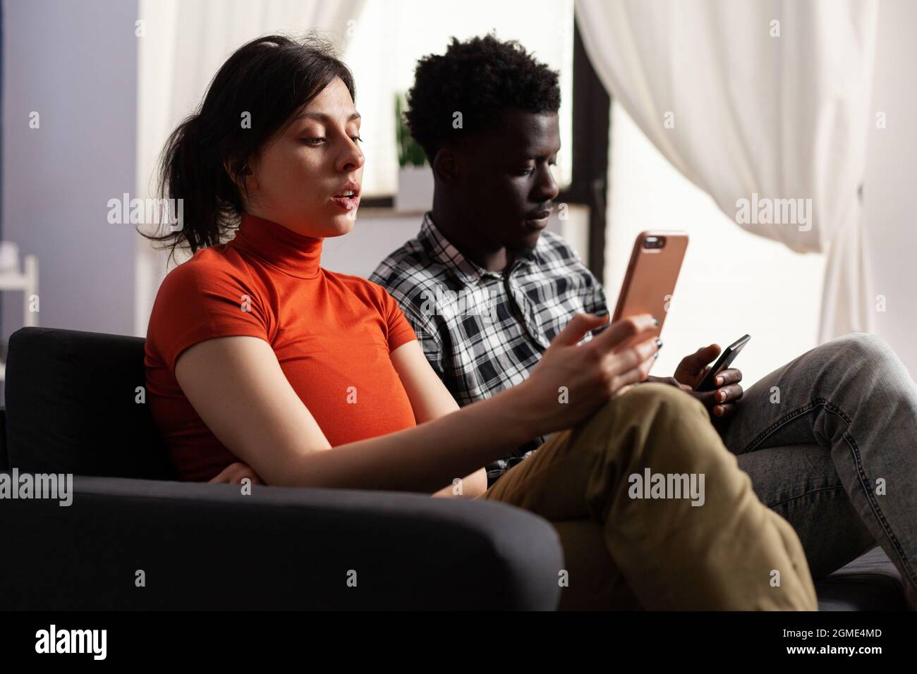 Primo piano della moderna coppia interrazziale utilizzando smartphone a casa. Amanti multietnici che detengono dispositivi digitali con tecnologia. Gente multirazziale che ha gadget con internet online. Foto Stock