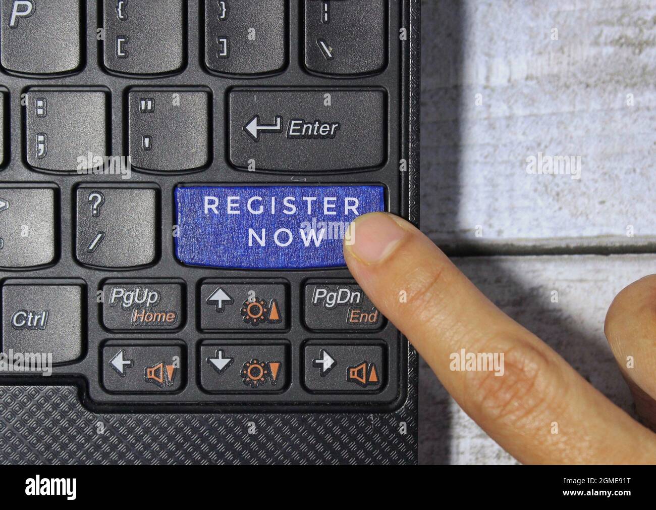 Premere con il dito un tasto blu etichettato REGISTER NOW con il simbolo sulla tastiera di un computer Foto Stock