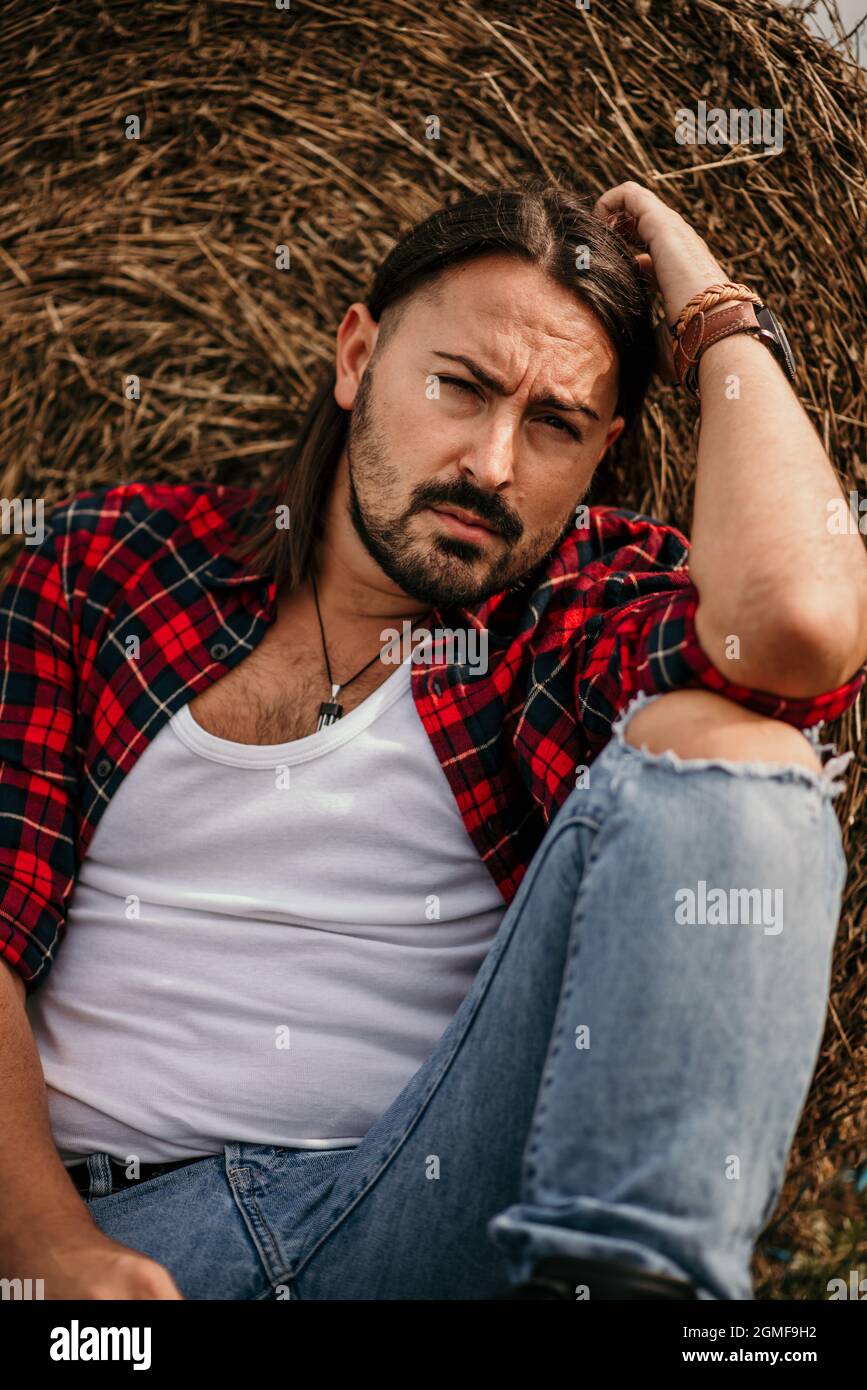 Giovane bel maschio serbo in una camicia in flanella e jeans strappati  seduti appoggiati su un pagliaio Foto stock - Alamy
